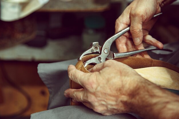 Aproveitando o processo de criação artesanal de calçados. Local de trabalho do designer de calçados. Mãos de sapateiro lidando com ferramenta de sapateiro, close-up