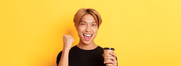 Aproximação da bomba de punho de um asiático bonito e energizado alegremente enquanto bebia café sorrindo excitado