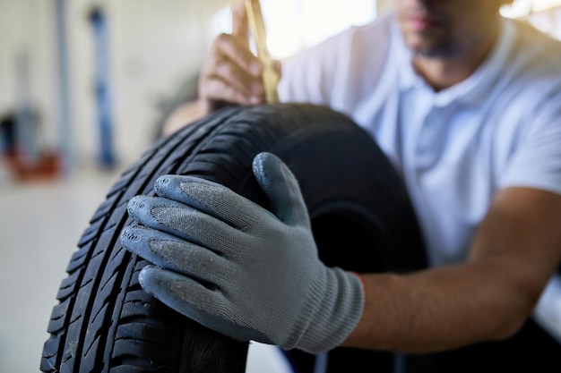 Aproximação do reparador de automóveis medindo a profundidade do pneu do carro na oficina de reparação de automóveis