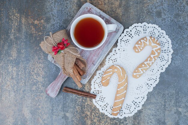 Aroma de chá em xícara branca com paus de canela e biscoito de Natal na mesa de mármore.