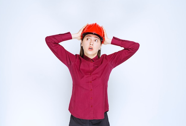 Arquiteta feminina de sucesso no capacete vermelho, segurando sua cabeça de frustração.