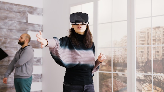 Arquiteta usando óculos de realidade virtual em um apartamento vazio e agente imobiliário falando com o cliente em segundo plano.