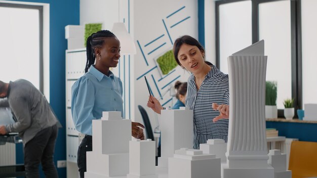 Arquitetos dando highfive e celebrando o progresso do projeto urbano com o modelo de construção. Colegas trabalhando em equipe na concepção e estrutura da construção, utilizando maquete no escritório.