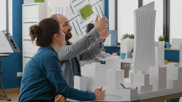 Arquitetos usando smartphone para projetar layout de construção com modelo de construção e plantas. Homem e mulher trabalhando com telefone celular para planejar a estrutura arquitetônica e o desenvolvimento.