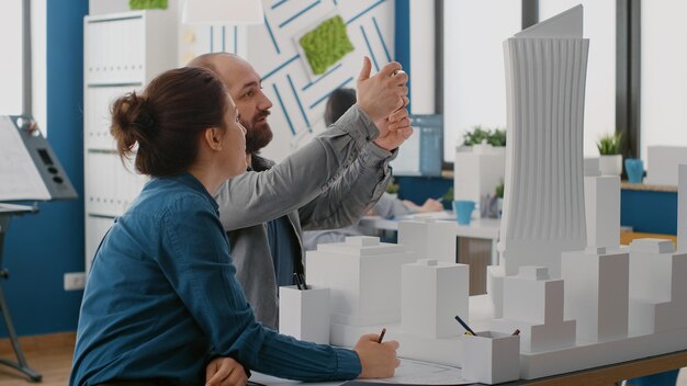 Arquitetos usando smartphone para projetar layout de construção com modelo de construção e plantas. Homem e mulher trabalhando com telefone celular para planejar a estrutura arquitetônica e o desenvolvimento.