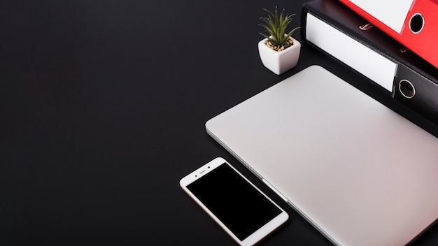 Arquivos em papel; planta de maconha; laptop fechado e smartphone em fundo preto