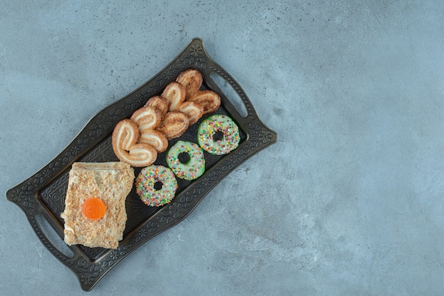 Arranjo de sobremesa com biscoitos escamosos, uma fatia de bolo, donut e em uma bandeja ornamentada em superfície de mármore