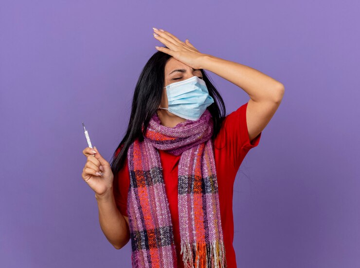 Foto grátis arrependendo-se de uma jovem caucasiana doente usando máscara e lenço segurando um termômetro, colocando a mão na cabeça com os olhos fechados, isolado na parede roxa com espaço de cópia