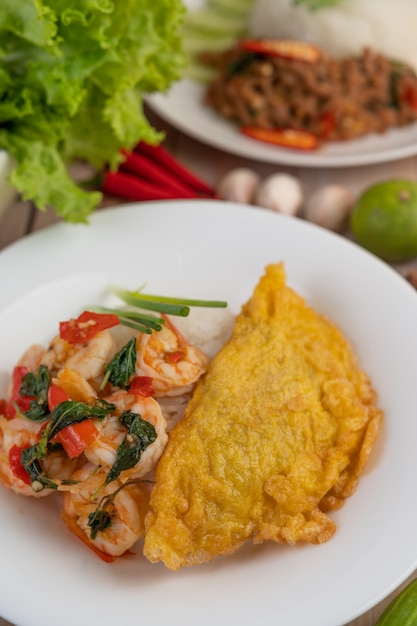 Arroz coberto com camarão e omelete em um prato branco.