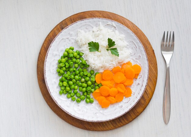Arroz cozido com legumes e salsa no prato na placa de madeira