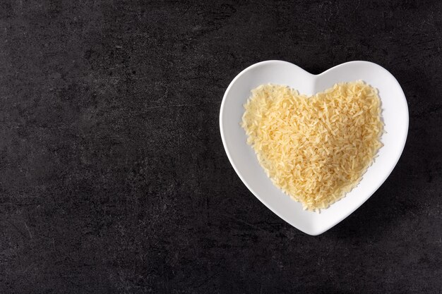 Arroz cru no prato em forma de calor em fundo preto