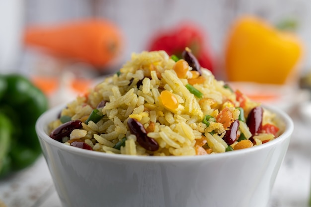 Arroz frito misto em uma xícara sobre um piso de madeira branco.