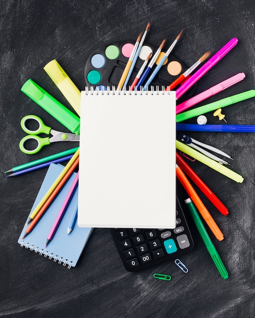 Artigos de papelaria coloridos, tintas, calculadora sob notebook em fundo cinza