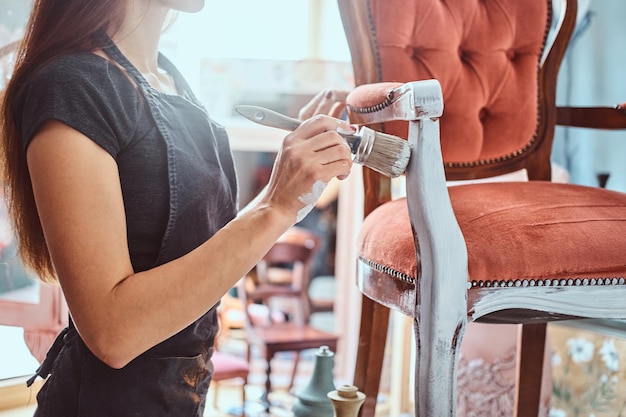 Artista feminina na cadeira vintage de pintura avental na cor branca com pincel na oficina.