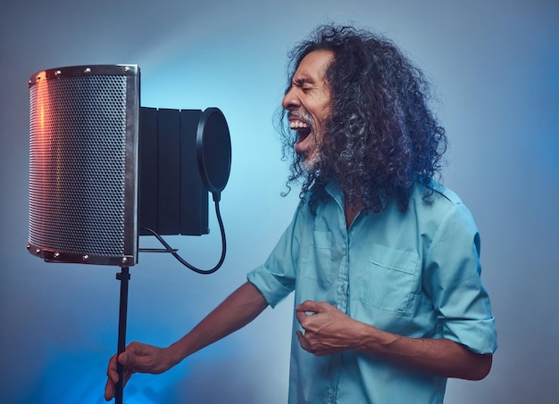 Foto grátis artista vocal africano canta uma música em voz alta ao lado de um condensador de microfone. isolado em um fundo azul.