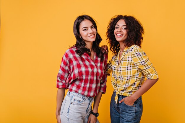 As amigas vestem camisetas semelhantes para parecerem fofas na sessão de fotos. Retrato de alegre morena de olhos castanhos.