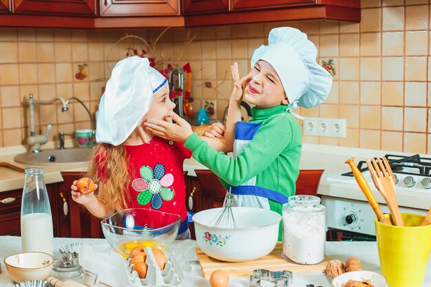 As crianças engraçadas da família feliz estão preparando a massa, assar biscoitos na cozinha