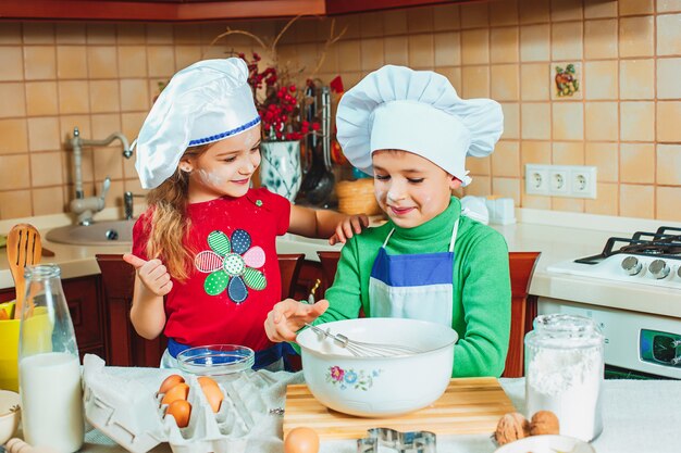 As crianças engraçadas da família feliz estão preparando a massa, assar biscoitos na cozinha