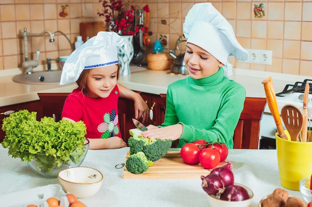 As crianças engraçadas da família feliz estão preparando uma salada de legumes fresca na cozinha