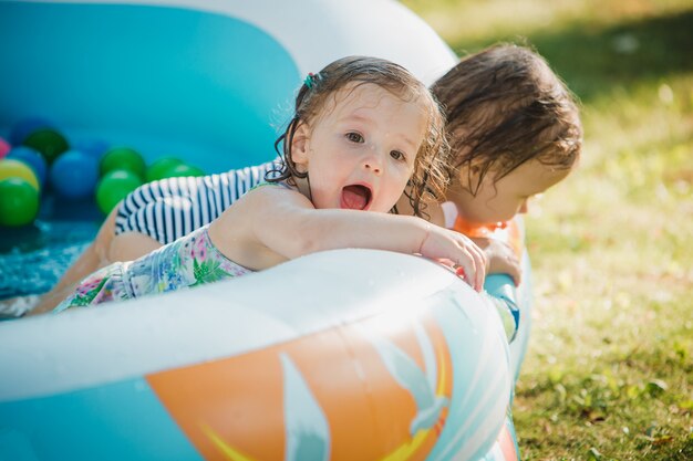 As duas meninas brincando com brinquedos na piscina inflável no dia ensolarado de verão