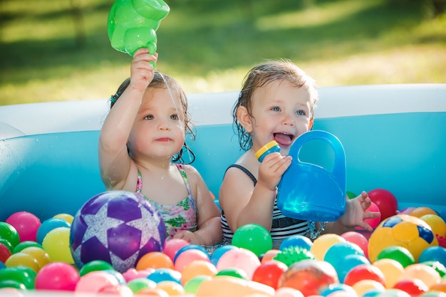 As duas meninas brincando com brinquedos na piscina inflável no dia ensolarado de verão