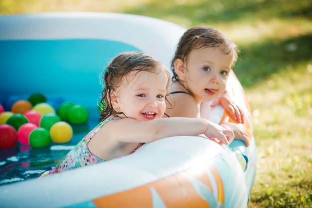 As duas meninas brincando com brinquedos na piscina inflável no dia ensolarado de verão