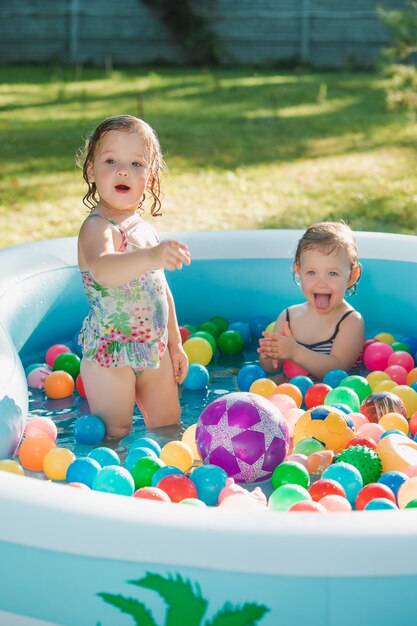 As duas meninas de dois anos de idade brincando com brinquedos na piscina inflável no dia ensolarado de verão