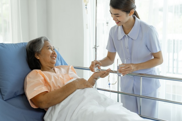 As enfermeiras são muito bem cuidadas, dão remédio a pacientes idosos em leitos hospitalares, sentem felicidade - conceito de paciente sênior de medicina e saúde