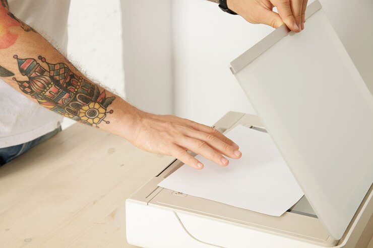Foto grátis as mãos abrem uma bandeja do scanner e colocam a folha de papel para digitalizar um documento dentro de um dispositivo eletrônico multifuncional, isolado na mesa de madeira branca,
