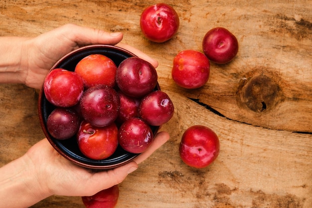 As mãos da menina seguram um prato com ameixas sobre uma mesa rústica de madeira vista de cima fundo de frutas com espaço para texto conceito de colheita de jardinagem agrícola