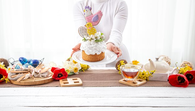 As mãos das mulheres estão segurando um bolo de Páscoa festivo, decorado com flores e detalhes brilhantes. O conceito de preparação para o feriado da Páscoa.