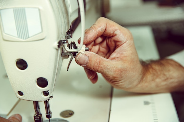 As mãos do homem e a máquina de costura. Oficina de couro. Têxtil vintage industrial. O homem na profissão feminina. Conceito de igualdade de gênero