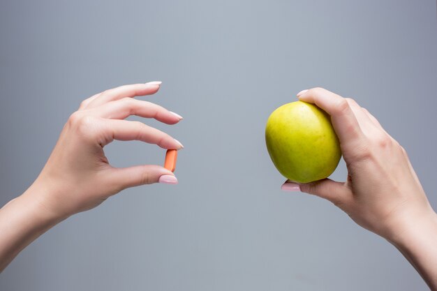 As mãos femininas com maçã e comprimidos em fundo cinza