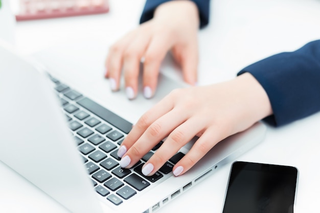 As mãos femininas no teclado do seu computador portátil