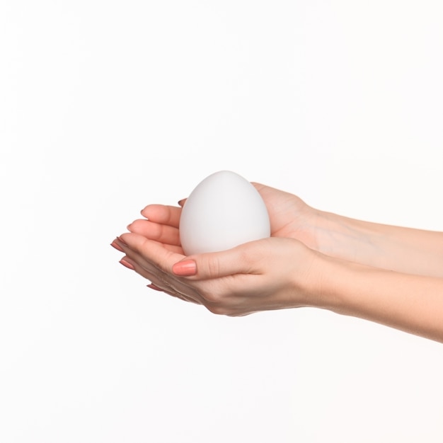 As mãos femininas segurando um ovo branco no branco.