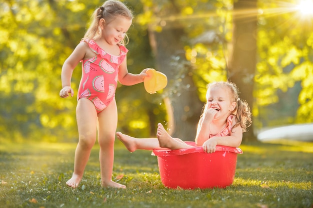 As meninas loiras bonitinha brincando com salpicos de água no campo no verão