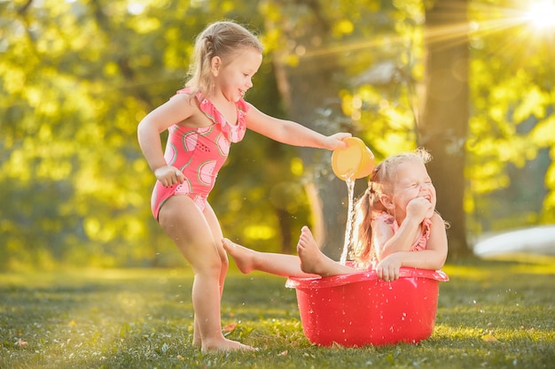 As meninas loiras bonitinha brincando com salpicos de água no campo no verão