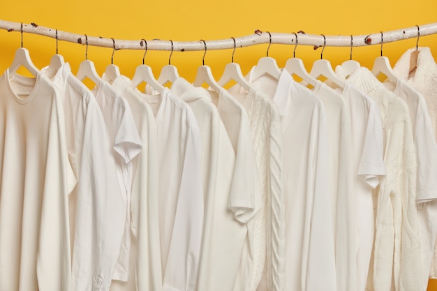 As mesmas roupas brancas em prateleiras de madeira no armário. coleção de roupas em cabides, isolada sobre fundo amarelo.