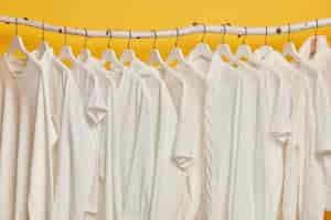Foto grátis as mesmas roupas brancas em prateleiras de madeira no armário. coleção de roupas em cabides, isolada sobre fundo amarelo.
