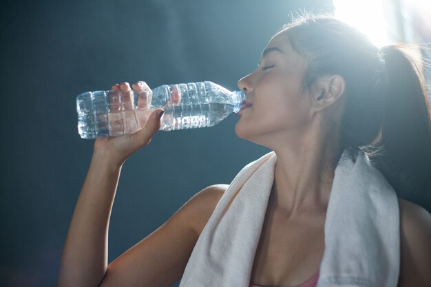 As mulheres após o exercício bebem água de garrafas e lenços no ginásio.