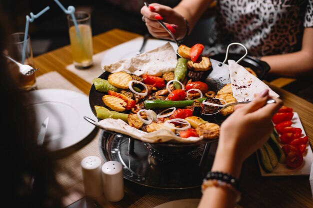 As mulheres da vista lateral comem um sábio de galinha tradicional azerbaijano do prato com batatas dos vegetais e pão de pão árabe