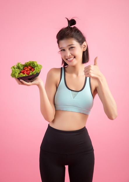 As mulheres jovens gostam de comer legumes em um rosa.