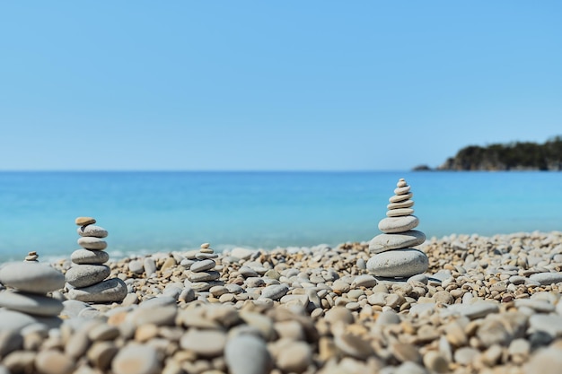 As pedras da pirâmide se equilibram na praia contra o fundo do mar e do céu Objeto em foco ideia de fundo desfocado de férias ou retuíte à beira-mar
