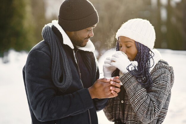 As pessoas caminham lá fora. Dia de inverno. Casal africano com café.