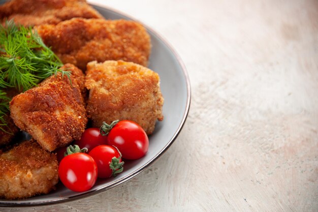 As saborosas asas de frango com verduras e tomates em frente ao prato na luz