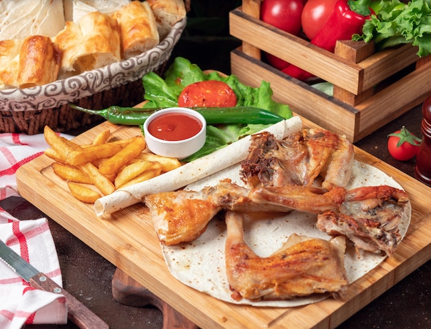 Asas de frango assado com batatas fritas em panela com legumes e ketchup na placa de madeira