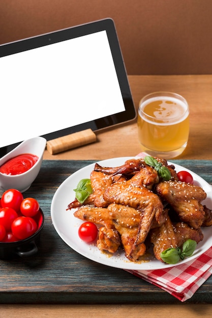 Asas de frango de ângulo alto no prato com tablet em branco