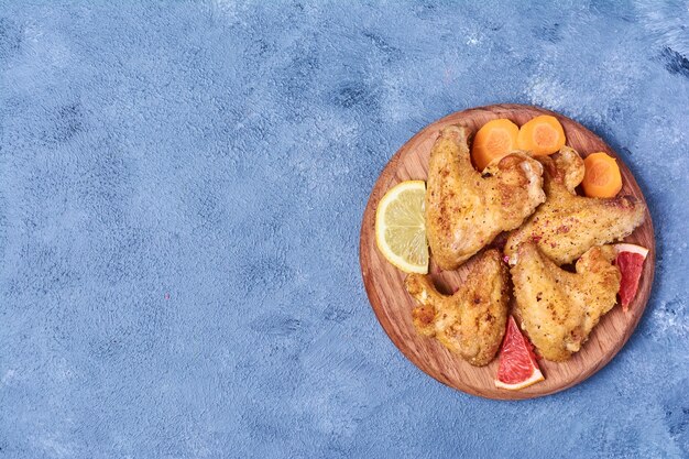 Asas de frango frito em uma placa de madeira em azul