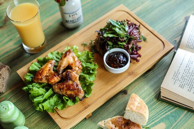 Asas de frango frito servidas com molho e ervas com suco de laranja