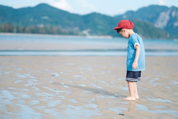 Asian boy andando na praia ao ar livre mar e céu azul